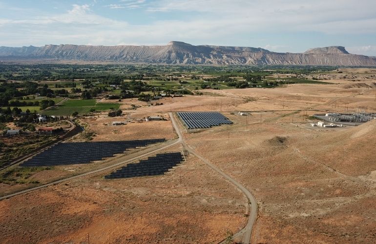 Pivot Energy's Mesa 2 Community Solar Garden in Colorado, with electricity transmission infrastructure visible in the background.