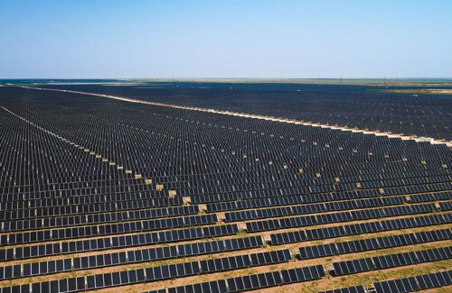 A large-scale solar project installed on arid land stretches to the horizon.